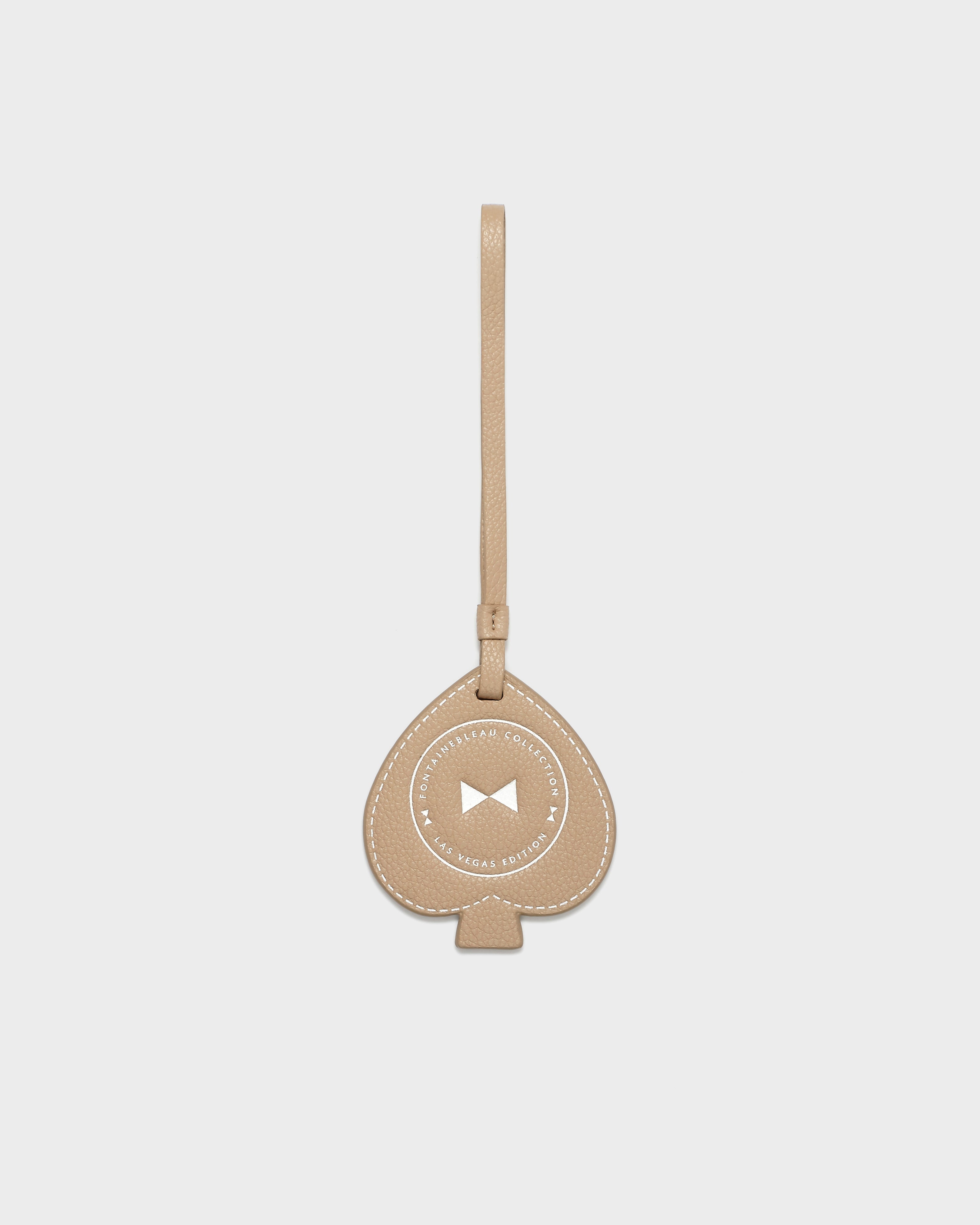 Luggage Spade Beige Bag Charm with Fontainebleau Collection Las Vegas Edition written in center, with a bowtie, in photo studio space